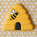 4 inch Bee Hive Metal Cookie Cutter in yellow with a bee design on a honeycomb patterned background.