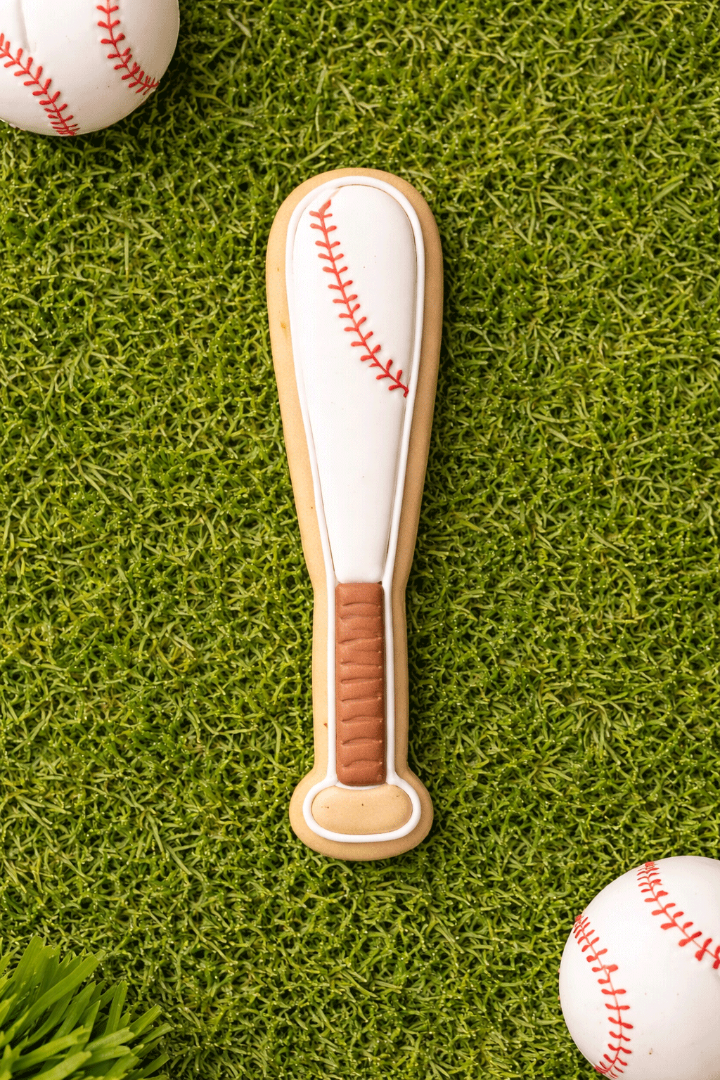 4.5 inch Baseball Bat Metal Cookie Cutter shaped cookie on grass with baseballs, perfect for sports-themed baking.