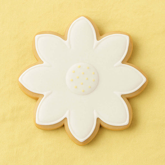 Decorative cookie shaped like a flower with white icing on a yellow background from a 2.25 inch Mini Daisy Flower Metal Cookie Cutter