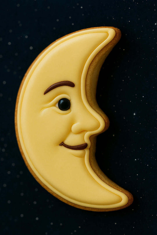 3 inch Man in the Moon Metal Cookie Cutter shaped cookie with yellow icing and a smiling face on a dark background.