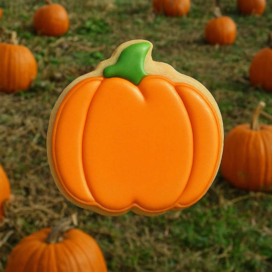 3 inch Pumpkin Metal Cookie Cutter shaped cookie with orange icing in a pumpkin patch background.