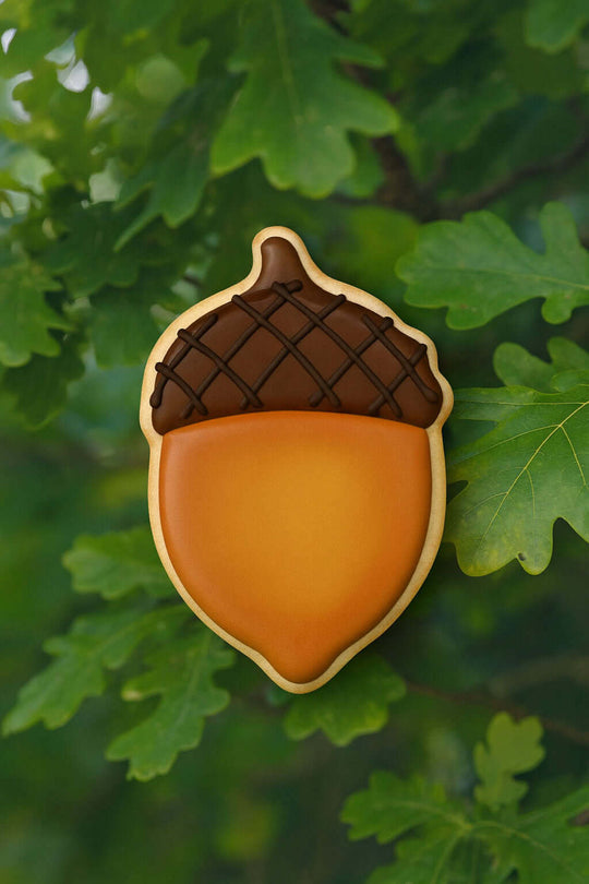 Acorn-shaped cookie with brown cap and orange body on green leaves from a 2.75 inch Acorn Metal Cookie Cutter