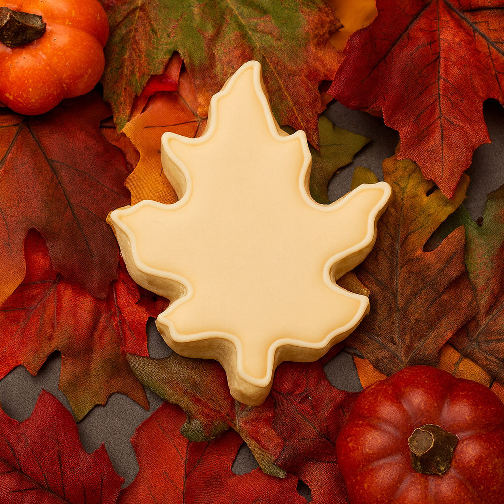 Oak leaf-shaped cookie on a bed of autumn leaves and pumpkins