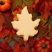 Oak leaf-shaped cookie on a bed of autumn leaves and pumpkins