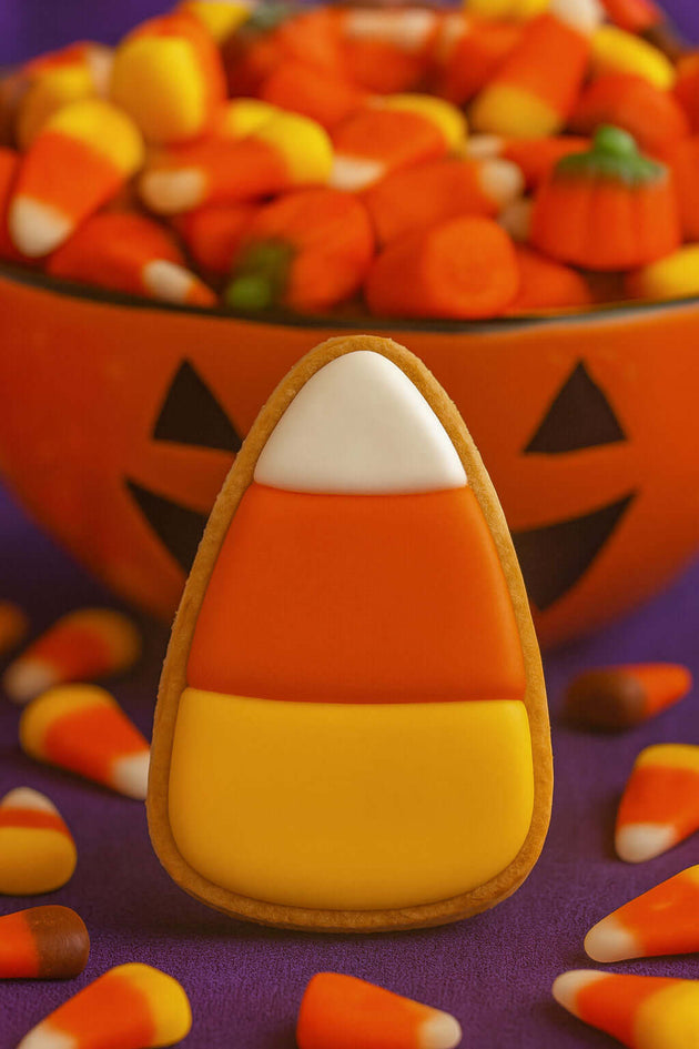 Halloween-themed cookie with candy corn design in front of a bowl of candy corn from a 3 inch Candy Corn Metal Cookie Cutter