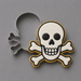A pirate skull and crossbones cookie cutter set on a neutral gray background, showing both the metal cutter and the shaped cookie with white icing, black details, and a gold border from a 3.25 inch Skull and Crossbones Metal Cookie Cutter