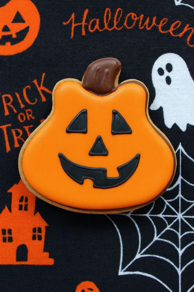 Pumpkin-shaped cookie with a face on a Halloween-themed background