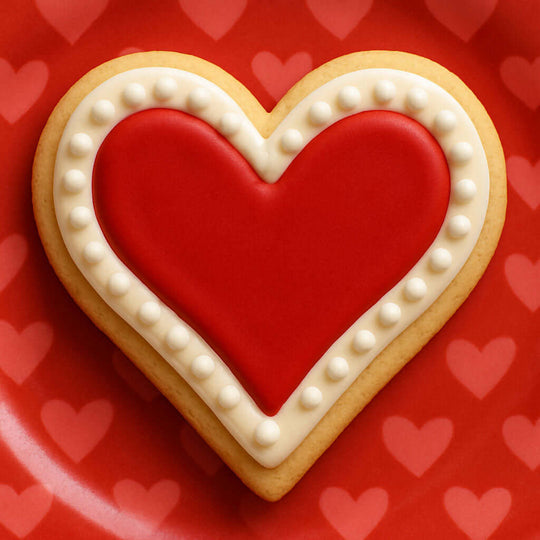 Heart-shaped cookie with white icing on a red background with heart patterns