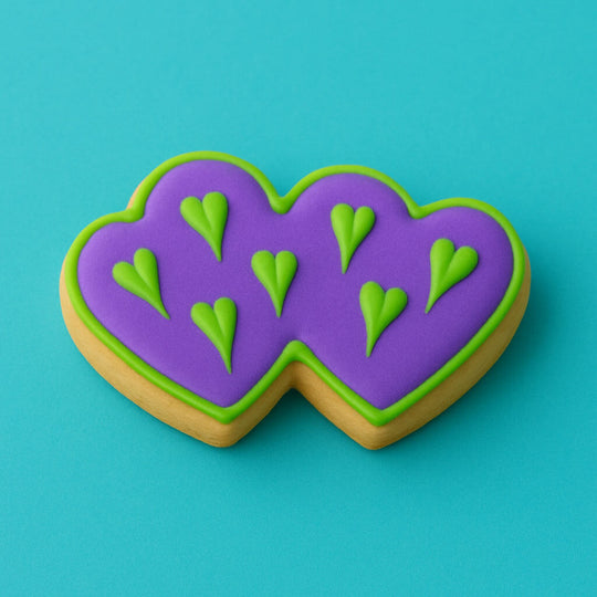 Heart-shaped cookie with purple icing and green heart decorations on a teal background from a 5 inch Double Heart Metal Cookie Cutter