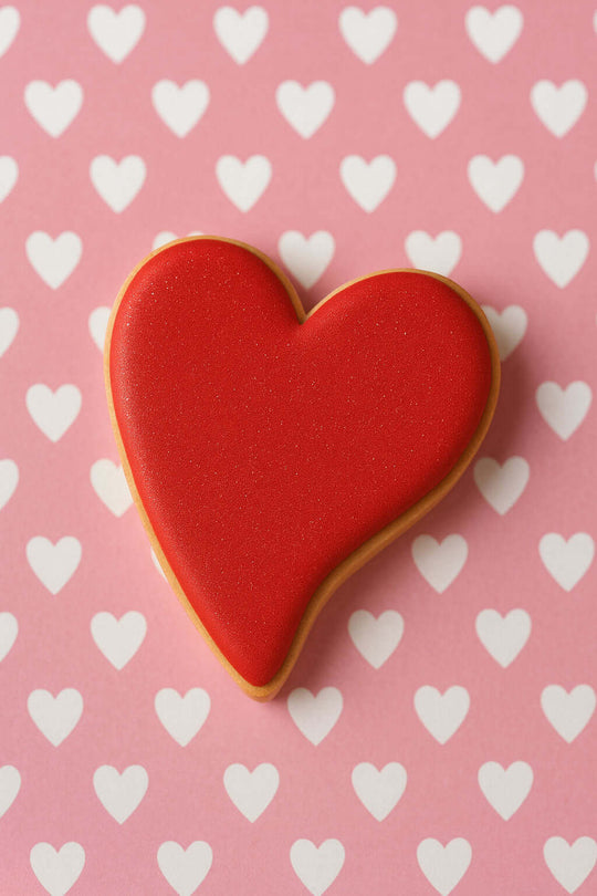 Red heart-shaped cookie on a pink background with white hearts