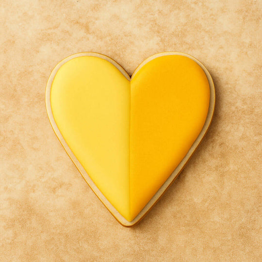 Heart-shaped cookie with yellow icing on a beige background from a 2 inch Heart Metal Cookie Cutter