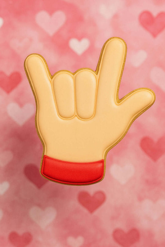 Hand sign cookie with red base on a pink background with heart shapes