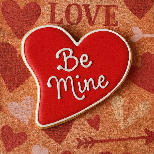 Heart-shaped cookie with 'Be Mine' text on a Valentine's Day-themed background
