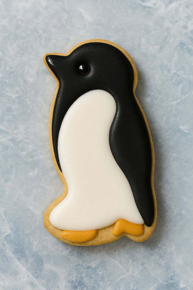 Penguin-shaped cookie with black and white icing on a textured gray background from a 3 inch Penguin Metal Cookie Cutter