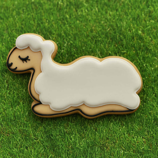 Sheep-shaped cookie on a grass background from a 3.25 inch Laying Down Lamb Metal Cookie Cutter