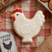 Chicken-shaped cookie on a red and white checkered tablecloth with eggs and straw from a 4 inch Chicken Hen Metal Cookie Cutter