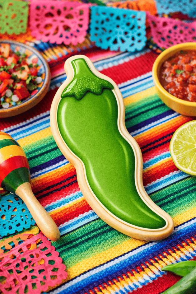 Green pepper-shaped cookie on a colorful striped tablecloth with salsa and limes from a 3 inch Chili Pepper Metal Cookie Cutter
