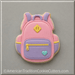 A pink and lavender sugar cookie cut in the shape of a backpack, decorated with yellow zipper details, a small light blue heart, and a yellow diamond emblem, set against a neutral gray background from a 3.5 inch School Backpack Metal Cookie Cutter