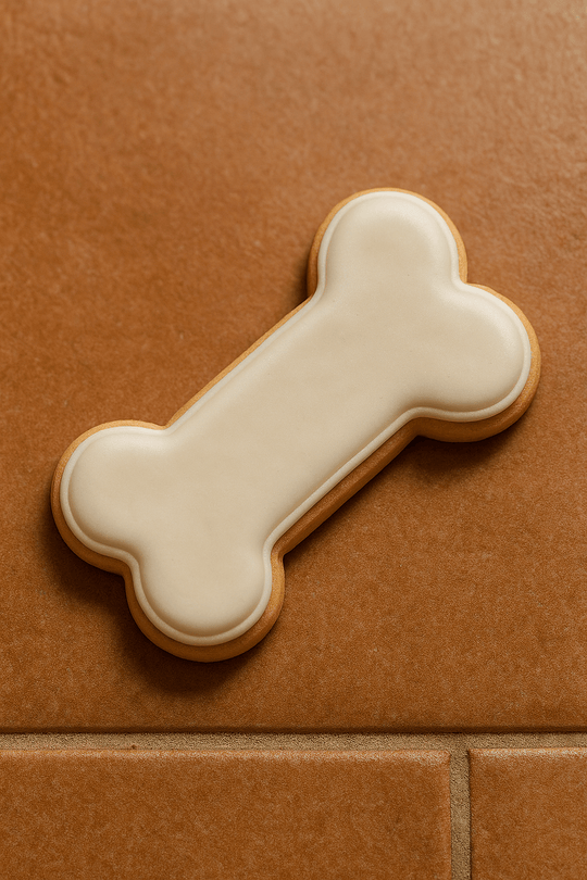 Dog bone-shaped cookie with white icing on a brown tile background from a 3 inch Dog Bone Metal Cookie Cutter