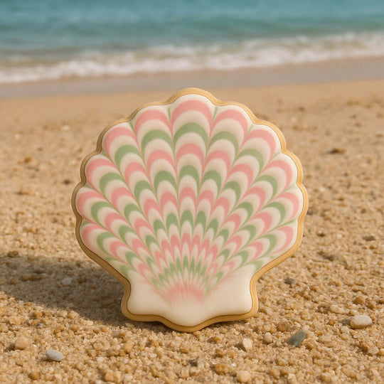 Shell-shaped cookie with pink and green pattern on a sandy beach