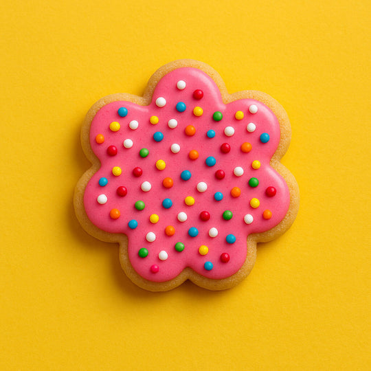 Colorful flower-shaped cookie with pink icing and sprinkles on a yellow background