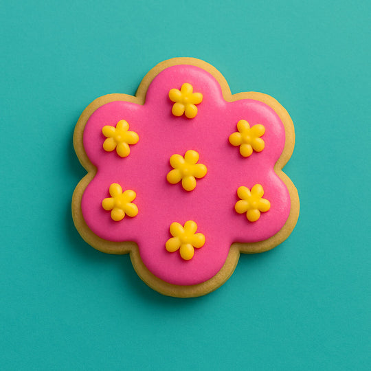 Decorative cookie with pink icing and yellow flowers on a teal background