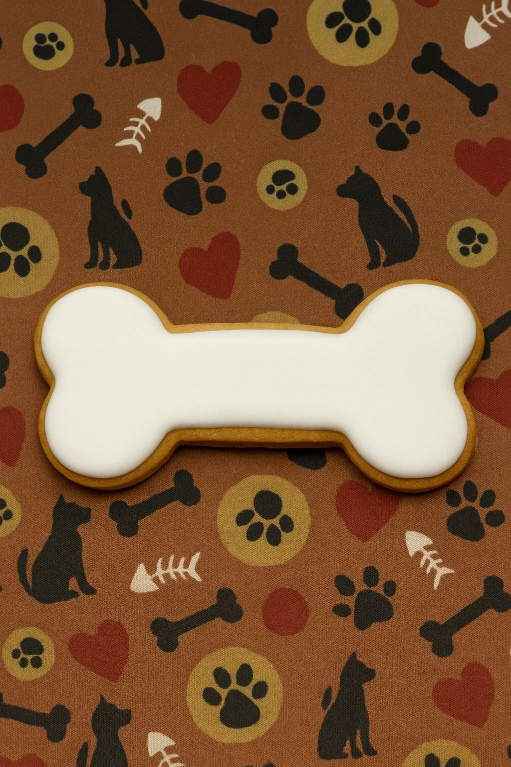 Bone-shaped cookie with white icing on a brown background with dog-themed patterns