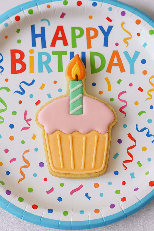 Colorful birthday plate with a cupcake cookie and candle on a white background
