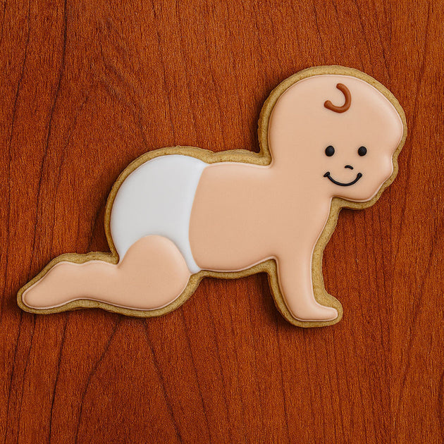 Cookie shaped like a crawling baby with a face on a wooden surface from a 5 inch Crawling Baby Metal Cookie Cutter