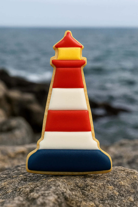 4.5 inch Lighthouse Metal Cookie Cutter shaped cookie with colorful icing against a coastal background.