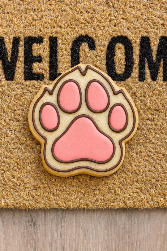 3 inch Dog Paw Metal Cookie Cutter shaped cookie on a welcome mat, perfect for animal lovers.