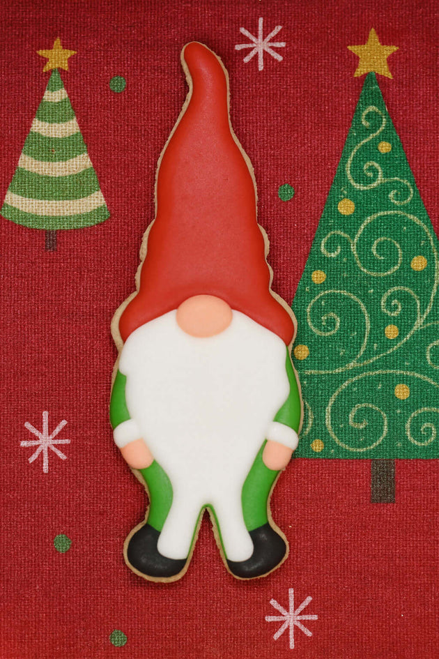 Decorative cookie shaped like a gnome with Christmas trees and snowflakes on a red background