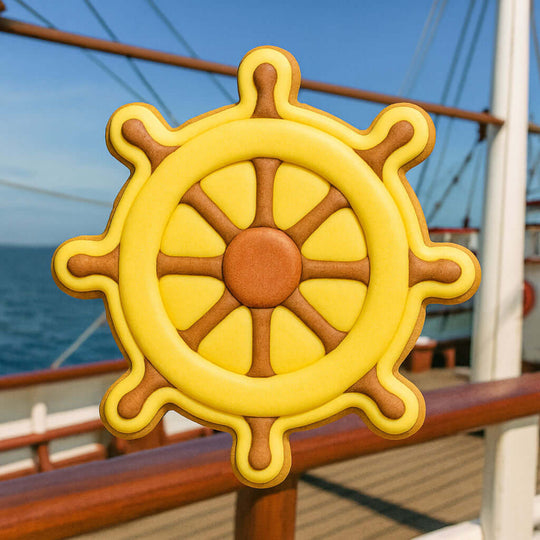 Close-up of a yellow and brown ship's wheel on a boat deck with water in the background