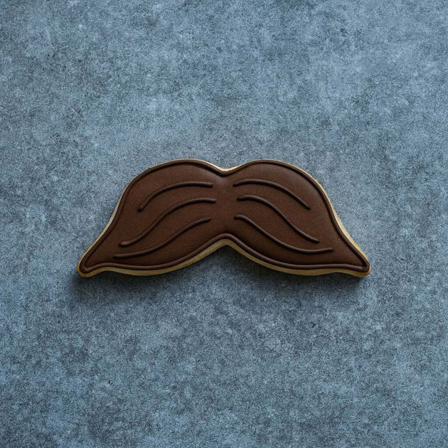 Brown mustache-shaped cookie on a gray textured background from a 5 inch Mustache Metal Cookie Cutter