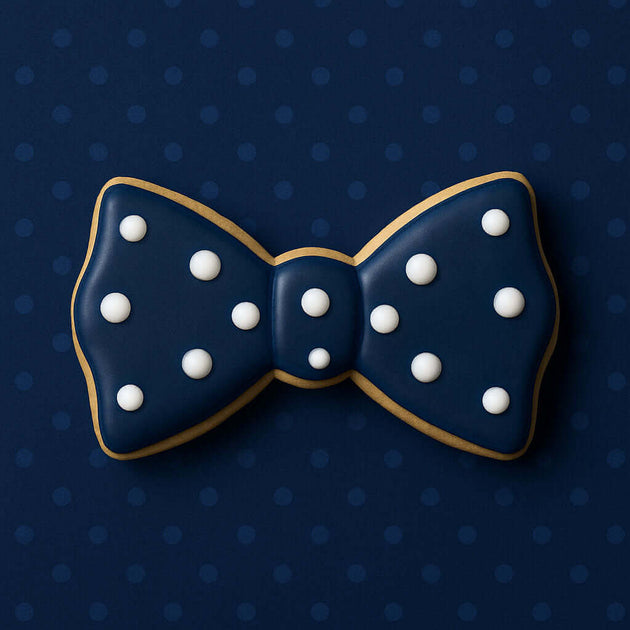 5 inch Bow Tie Metal Cookie Cutter shaped cookie decorated with white dots on dark blue background.