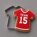 A red soccer jersey shaped sugar cookie with white icing details reading 'TEAM 15', shown next to a metal cookie cutter on a smooth gray background from a 4 inch T Shirt Metal Cookie Cutter