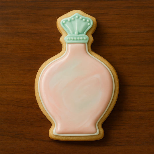Cookie shaped like a perfume bottle with pink body and green cap on a wooden surface