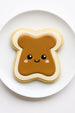 Cookie shaped like a piece of toast with peanut butter, on a white plate.