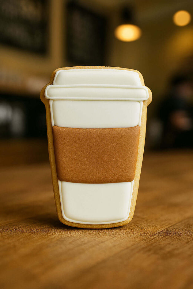 Cookie shaped like a coffee cup with a white lid and brown body on a wooden surface from a 4 inch Paper Coffee Travel Mug Metal Cookie Cutter