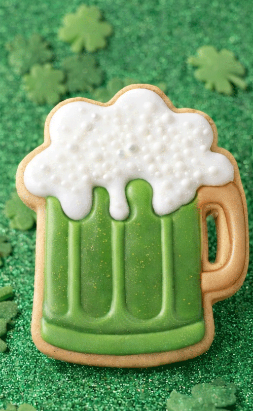 Cookie shaped like a beer mug with white foam on a green background with shamrocks from a 4 inch Root Beer Mug Metal Cookie Cutter