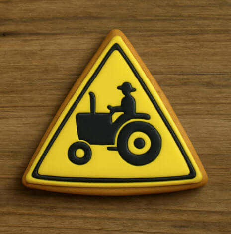 Triangular warning sign with a tractor and person icon on a wooden surface