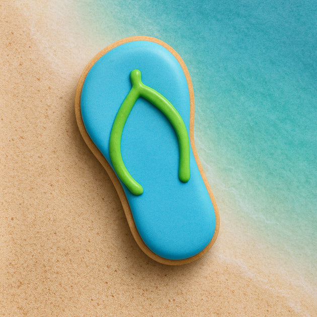 Cookie shaped like a flip-flop with blue icing and green strap on a beach background