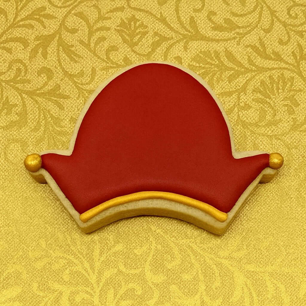 Decorative cookie shaped like a red hat with gold accents on a yellow patterned background