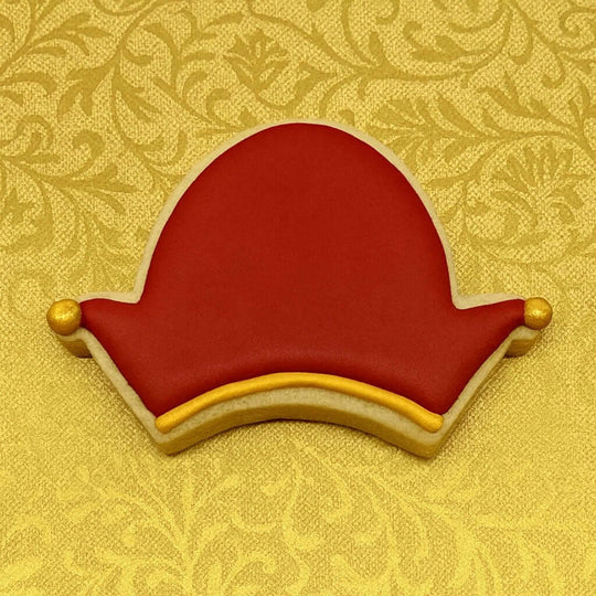 Decorative cookie shaped like a red hat with gold accents on a yellow patterned background