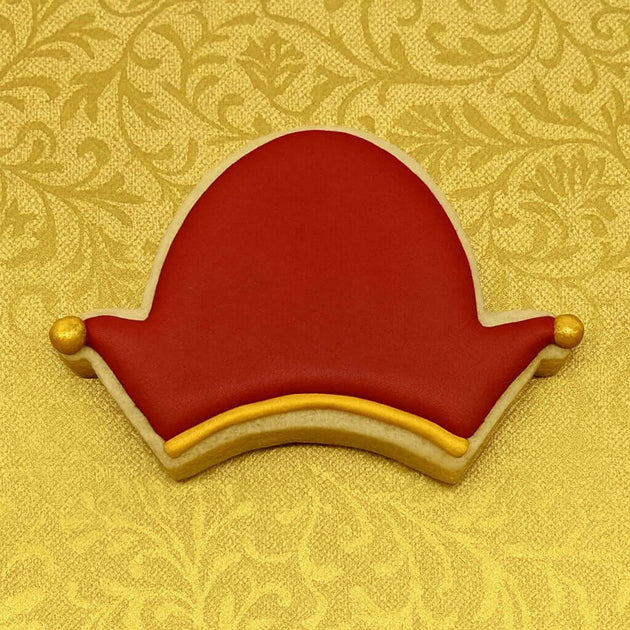 Decorative cookie shaped like a red hat with gold accents on a yellow patterned background