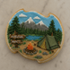 Decorative cookie shaped like a plaque with a camping scene, including a tent, campfire, and mountains from a 4.75 inch Plaque or Frame Metal Cookie Cutter