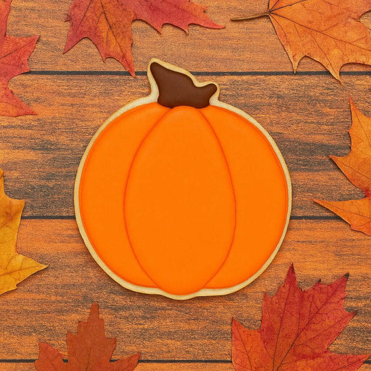 Pumpkin-shaped cookie on a wooden surface with autumn leaves from a 4 inch Pumpkin Metal Cookie Cutter