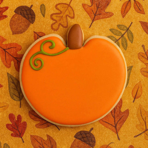 Pumpkin-shaped cookie with orange icing and chocolate acorn on a fall leaf pattern background from a 4 inch Pumpkin Metal Cookie Cutter