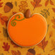 Pumpkin-shaped cookie with orange icing and chocolate acorn on a fall leaf pattern background from a 4 inch Pumpkin Metal Cookie Cutter