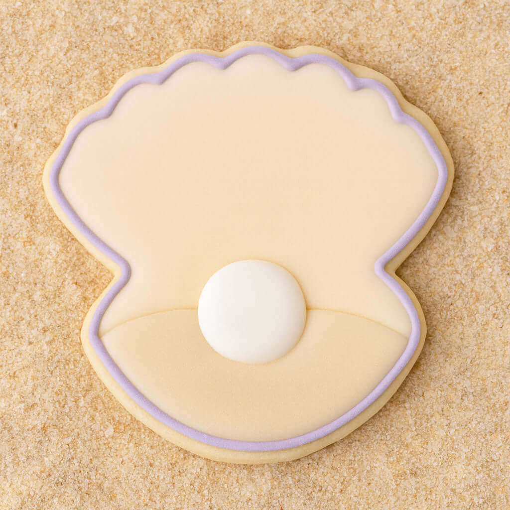 Clam shell with pearl  outlined in purple cookie on a sandy background from a 4 inch Oyster Clam Shell Metal Cookie Cutter